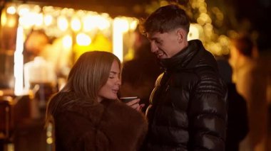 Paris 'te genç bir çift, gece boyunca Noel pazarında sıcak içeceklerden zevk alır. Kadın ve erkek, romantik bir kış sahnesi sergiliyor ve gülümsüyor..