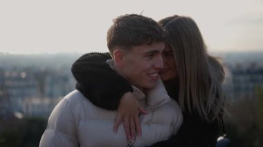 Romantik bir çift, arka planda Paris silueti ile kucaklaşır kadın, sevgi ve sevgi gösteren adama sarılır. Sıcak bir ışıkla çekilir. Romantizm ve bağın bir anını yakalar..