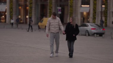 Genç bir çift, gün batımında Paris 'te bir şehir meydanında el ele yürür. Aşıklar Avrupa' da birlikte dolaşırken elde çekilen fotoğraf romantik atmosferi yakalar..