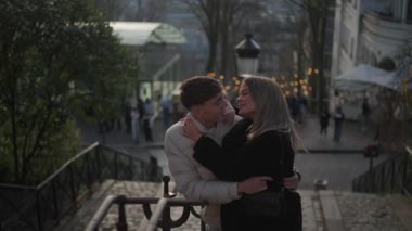 Genç bir çift Paris 'te Montmartre' nin merdivenlerinde sarılıyor. Aşıklar Sacre-Coeur Bazilikası 'nın bulanık arka planıyla sarılıyorlar..