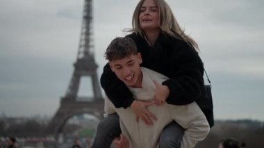 Genç bir çift, arka planda Eyfel Kulesi ile Paris 'te sırt sırta binmekten zevk alır. Mutlu adam, kadını sırtında taşıyarak romantik bir seyahat sahnesinde kameralı çekimler yapar..
