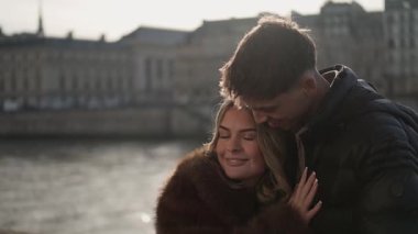 Paris 'te genç bir çift, Fransa' da Seine Nehri ve şehir binalarıyla kucaklaşırken, arka planda görülen sahne, Avrupa 'daki seyahat deneyimleri sırasında bir aşk ve mutluluk anı yakalar..