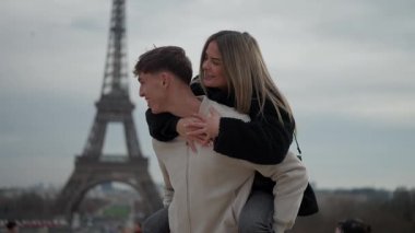Genç bir çift Paris 'te romantik bir anın tadını çıkarıyor. Erkek, kadına arka planda Eyfel Kulesi ile sırt sırta veriyor. Çift gülümsüyor ve sevgisini ve sevgisini sergiliyor..