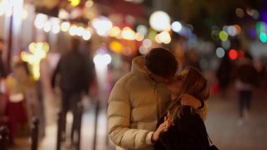 Romantik bir çift gece Paris 'te bir öpücüğü paylaşıyor şehir ışıkları bulanık bir arka plan oluşturuyor ve samimi ve sevgi dolu anı ekliyor bu sahne, bir Avrupa kentsel ortamında aşkın ve sevginin özünü yakalıyor..
