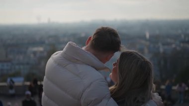 Romantik bir çift, arka planda Paris şehrinin siluetini kucaklıyor. Kadın ve erkek, Paris 'in manzarasının tadını çıkarıyorlar..