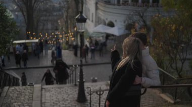 Paris 'te bir çift Montmartre' dan manzaraya bakıyor. Arka planda yürüyen insanlarla romantik bir sahne. Çekim, şehri ve çifti bir arada tutan bir fotoğraf..