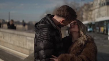 Paris 'teki genç bir çift, arka planda güneşli bir günde Paris mimarisinde kadın ve erkek birbirlerine sevgiyle sarılıp bakıyorlar..