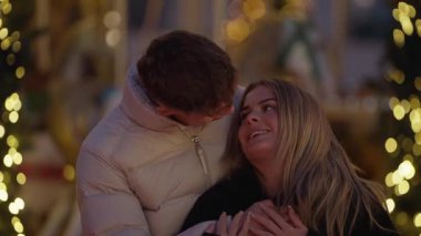 Genç bir çift Paris 'te bir atlıkarıncanın yanında kucaklaşır aşıklar, arka planda Bokeh ışıkları ile romantik ve şenlikli bir atmosfer yaratarak, tatil romantizminin ve seyahatin ruhunu yakalar..