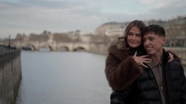 Paris 'te Seine Nehri ve Pont Neuf Köprüsü' nün arka planında sevgi dolu bir çift, ikonik Işık Şehri 'nde bir aşk ve şefkat anı yakalar..