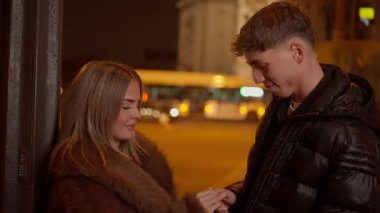 Arc de Triomphe arka planda görünürken genç bir çift gece Paris 'te el ele tutuşurken yavaş çekim aşıklar arasında aşk şehrinde kucaklaşırken romantik bir anı yakalar..