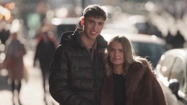 Genç bir çift Paris 'te bir şehir caddesinde bir portre için poz veriyor. Arka planda arabalarla ve yürüyen insanlarla ilgili yumuşak bir bokeh etkisi var. Çift kucaklaşıyor ve gülümsüyor. Sıcak ve sevgi dolu bir sahne yaratıyor..