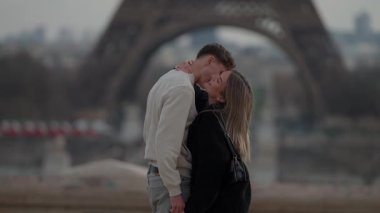 Paris 'te arka planda Eyfel Kulesi olan romantik bir çift öpücüğü. Yavaş çekim klibi, bulutlu bir günde aşıkların kucaklaşıp seyahat romantizmini ve sevgisini aktardığı tarihi bir anı yakalar..