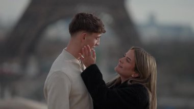 Paris 'te, arka planda Eyfel Kulesi olan romantik bir çift kadın, birbirlerine sevgi ve sevgiyle bakarken erkeğin gözlerine hafifçe dokunur.