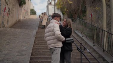 Genç bir çift Paris 'te Montmartre' nin merdivenlerinde sarılıyor. Aşıklar, arka planda Paris mimarisi olan kaldırım taşından bir merdivende birbirlerine sevgi ve romantizm gösteriyorlar..