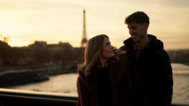 Paris 'te Eiffel Kulesi' nin arkasında altın bir günbatımında görülebilen romantik bir çift duruyor. Genç adam ve kadın birbirlerine sevgi ve sıcaklıkla bakıyorlar..