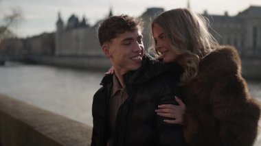 Paris 'te genç bir çift, Seine Nehri' nde ve arka planda tarihi binalarla kucaklaşıyor. El kamerası, aşıkların şehirde geçirdikleri zamanın keyfini çıkarırken romantik anı yakalıyor..