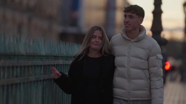 Gün batımında Paris Fransa 'nın Seine nehri boyunca yürüyen genç bir çift, şehrin atmosferinin tadını çıkarırken elde taşınan fotoğraf romantik bir havayı yakalar. Seyahat yaşam tarzı veya ilişki içeriği için ideal.