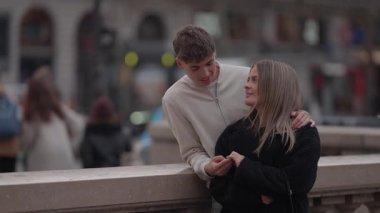 Paris 'te genç bir çift bir köprüde duruyor birbirlerine sevgiyle sarılıyorlar ve bakıyorlar şehir manzarası arka planda yumuşak bir odak ve sığ bir alan derinliği ile görülebiliyor..