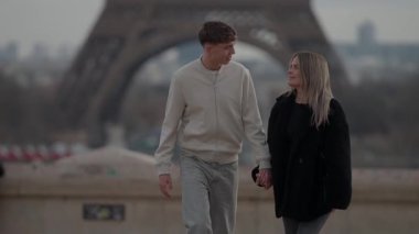 Paris 'te arka planda Eyfel Kulesi ile el ele yürüyen bir çift romantik sahne ikonik şehirde aşkın ve seyahatin özünü yakalar..