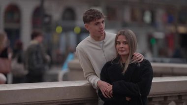 Genç bir çift Paris 'te bir köprüde kucaklaşıyor bulanık şehir arkaplanı romantik atmosfere ekliyor kadın ve erkek birlikte Avrupa' da vakit geçiriyorlar..