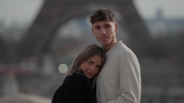 Paris 'te genç bir çift sarılıyor. Arka planda Eiffel Kulesi bulanıklaşıyor. Romantizm, seyahat ve yakınlık uyandırıyor..