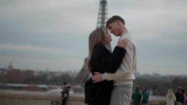 Arka planda Eyfel Kulesi ile Paris 'te genç bir çift kucaklaşırken görülüyor. Aşıklar Avrupa' nın manzaralı şehrinde birbirlerine sarılıp sevgisini dile getiriyorlar..