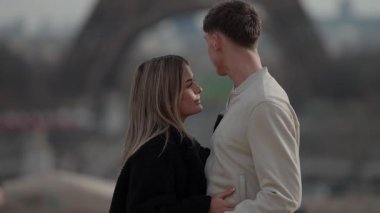 Arka planda Eiffel Kulesi 'nin bulanıklaştığı Paris' te romantik bir çift kucaklaşır. Romantizm seyahati ve turizmi taşır. Sığ alan derinliği ve yumuşak odaklar rüya gibi bir atmosfer yaratır..