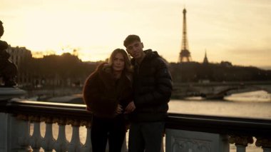 Günbatımında Paris 'teki Eyfel Kulesi' nin önünde bir çift poz veriyor. Video, altın saat boyunca el kamerasıyla romantik bir tatil anını yakalıyor..