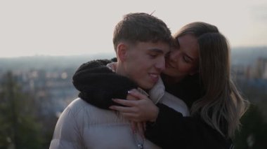 Genç bir çift, arka planda Paris siluetine sevgiyle sarılır kadın, sevgi ve bağlarını gösteren adama sarılır ve öper..