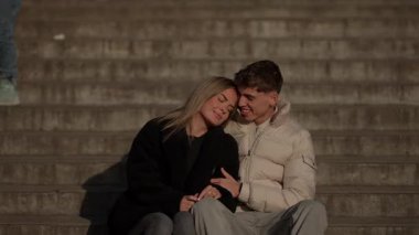 Genç bir çift Paris 'te basamaklarda oturuyor romantik bir anın tadını çıkarıyorlar âşıklar sarılıyor ve gülümsüyor altın saat ışığında sevgi ve mutluluk gösteriyorlar..