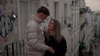 Romantik bir çift, Paris 'te bir sokakta el ele tutuşup birbirlerine aşkla bakıyorlar. Fotoğraf, el kamerasıyla çekiliyor ve binaların önünde grafiti yapan çifti gösteriyor..