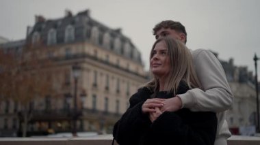 Genç bir çift Paris Fransa 'da kucaklaşırken görülüyor arka plan bulanıklaşıyor çiftin sevgisine odaklanıyor çekim, bulutlu bir havada romantik anın orta açısını yakalıyor..