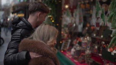 Paris 'te romantik bir çift Noel pazarının vitrinine bakıyor. Erkek kürk giyen kadına sarılıyor. Sahne, tatil alışverişini ve kış yolculuğunu çağrıştırıyor..