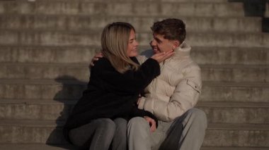Genç bir çift Paris 'te taş basamaklarda kucaklaşırken erkek ve kadın açık havada oturmuş doğal ışıkta romantik bir anı paylaşıyorlar. Gülümsüyorlar ve gülüyorlar birlikte geçirdikleri zamanın tadını çıkarıyorlar..