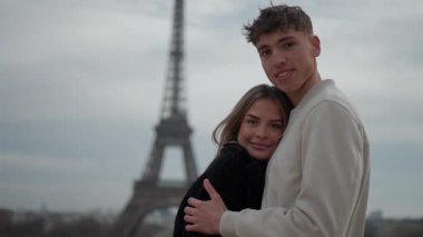 Genç bir çift Paris 'te arka planda Eyfel Kulesi ile sarılıyor. Aşıklar aşk şehrinde birlikte vakit geçiriyorlar ve eğleniyorlar..