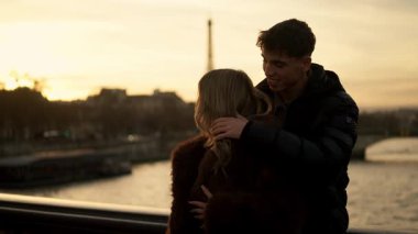 Romantik bir çift Paris 'te arka planda görünen Eyfel Kulesi' ne sarılır. Gün batımında altın saat ışığı sıcak ve davetkar bir atmosfer yaratır.