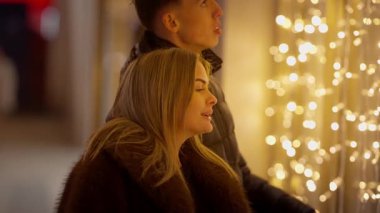 Genç bir çift gece Paris 'te vitrinlere bakıyor kadın ve erkek bir mağazanın vitrininde Noel ışıklarına bakıyor sahne şehirdeki romantik bir randevuyu yakalıyor.