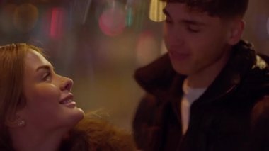 Genç bir çift gece Paris 'te birlikte vakit geçirirken görülüyor. El kamerasıyla çekilen fotoğraf, arka planda bokeh ışıkları ve gülücükler eşliğinde romantik atmosferi yakalıyor..