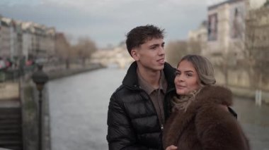 Genç bir çift Paris 'te bir köprüde Seine Nehri ve Pont Neuf Köprüsü' nün arka planında görünür bir şekilde kucaklaşır..