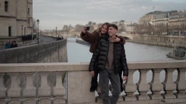 Paris 'te bir çift selfie çekiyor kadın erkeğin sırtında sarılıyor Seine nehri ve Paris binaları arka planda görünüyor klipte seyahat aşkı ve romantik bir yaşam tarzı görülüyor.