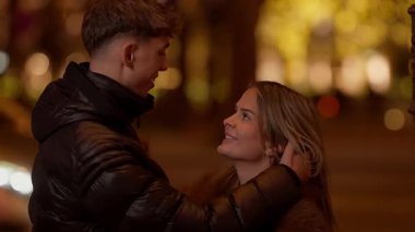 Romantik bir çift öpücükler Paris 'te gece Fransa' da Genç aşıklar aşk şehrinde sarılır arka planda yumuşak odaklı ışıklarla Aşk ve sevgiyi çağrıştırır.