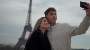 Genç bir çift Paris 'teki Eyfel Kulesi' nin önünde selfie çekiyor. Fransa 'daki el kamerası romantik tatillerini ve seyahat aşklarını yakalıyor. Arka planda ikonik bir dönüm noktası olan Avrupa' da turizm sahneleri sergileniyor..