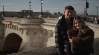 Bir çift Paris 'te bir köprüde sarılıyor. Arka planda Seine nehri var. Çift Avrupa' da romantik bir anın tadını çıkarıyor..