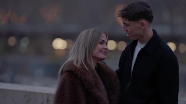 Paris 'te romantik bir çift alacakaranlıkta genç bir adam ve aşık bir kadın arka planda şehir ışıklarıyla aşıkların yavaş çekimleri ile birbirlerine bakıyorlar..