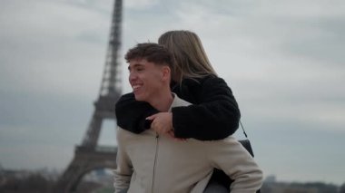 Mutlu bir çift, arka planda Eyfel Kulesi olan Paris 'te sırtında gezintiyle eğleniyor. Adam kameraya gülümsüyor. Bu sahne, ikonik şehirde seyahat ve turizmi ön plana çıkaran romantik bir tatil anını yakalıyor..