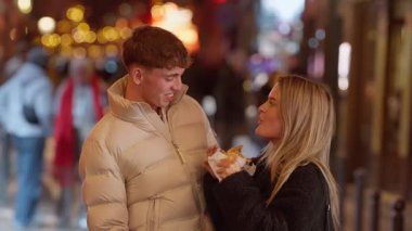 Genç bir çift Paris 'te kalabalık bir caddede akşam yemeğini paylaşıyor. Kadın erkeği besliyor. Bokeh ışıkları Avrupa' da romantik bir buluşmanın arka planında görülüyor..