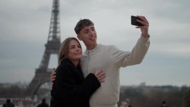 Genç bir çift, Paris 'teki Eyfel Kulesi' nde özçekim yapıyor. Aşıklar, arka planda ikonik simge olan bir fotoğraf için birbirlerine sarılıp poz veriyorlar. Bu klip seyahat ve romantizmin özünü yakalar..
