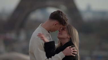 Genç bir çift Paris 'te Eiffel Kulesi' nin arka planında görünür bir şekilde sarılır yavaş çekim aşıklar şehrinde romantik bir an yakalar..