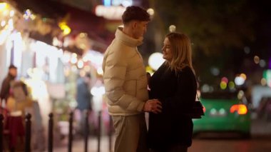 Genç bir çift gece Paris 'te bir sokakta kucaklaşır kadın ve erkek şehrin ışıklarıyla konuşur ve el ele tutuşur. Arka planda bokeh etkisi yaratır. Şehir ortamında romantik bir anı yakalar..