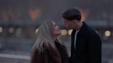 Genç bir çift, akşam karanlığında Paris 'te samimi bir anı paylaşıyor. Aşıklar birbirine bakıyor. Arka planda şehir ışıkları bulanık..